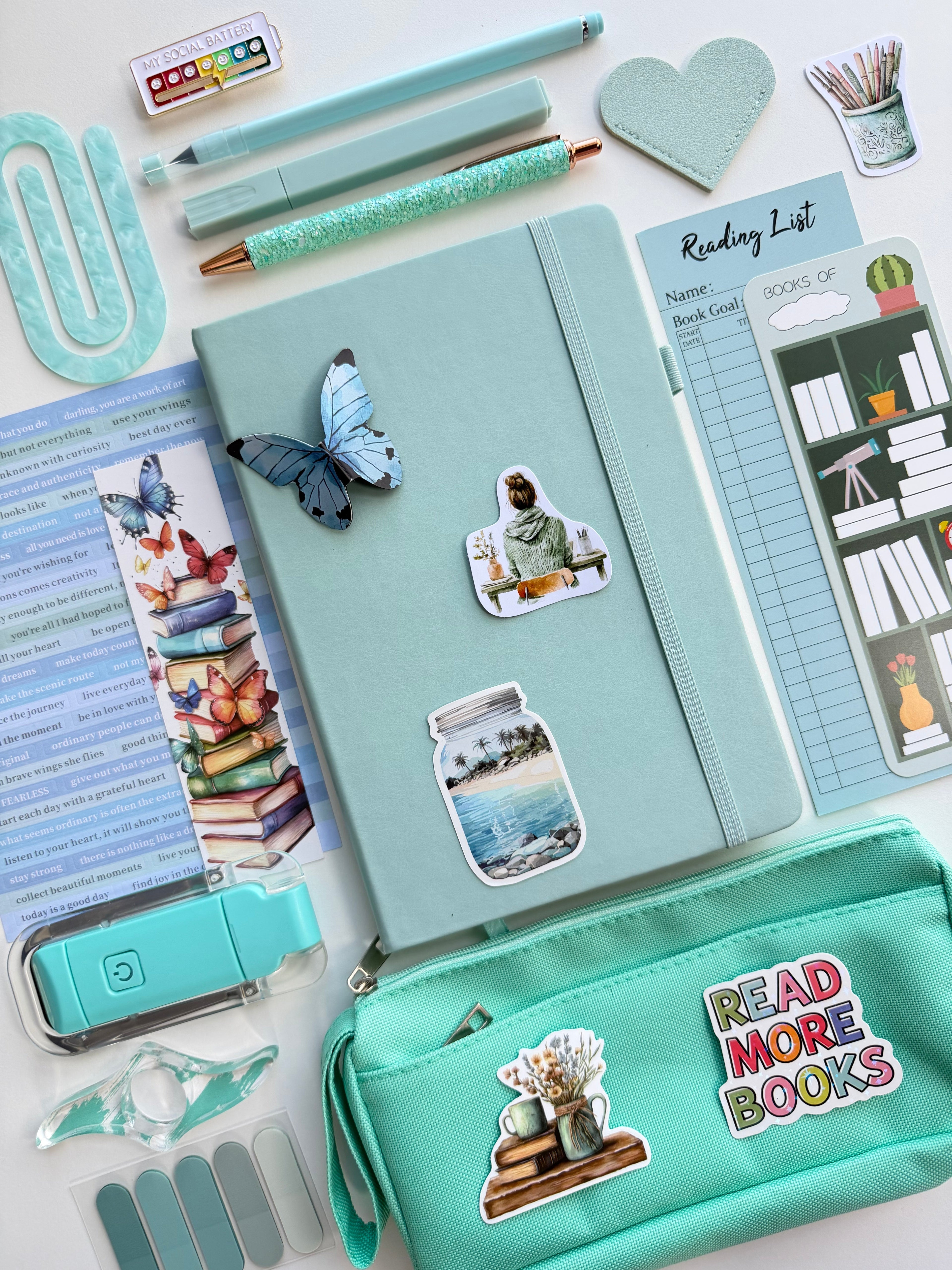 Collection of stationery items including a notebook, pens, and a pencil case on a white background.