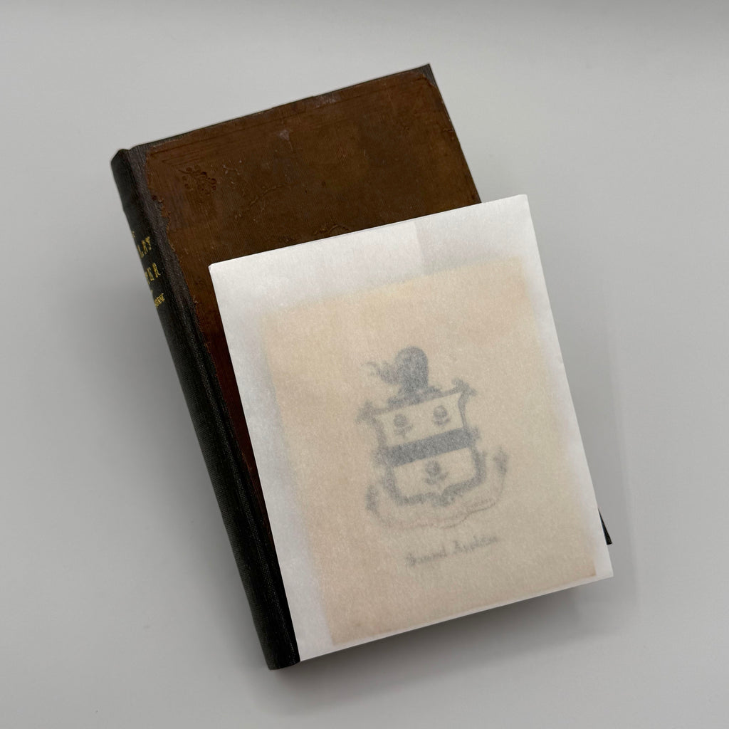 Brown book with a white paper cover featuring an emblem on a gray background