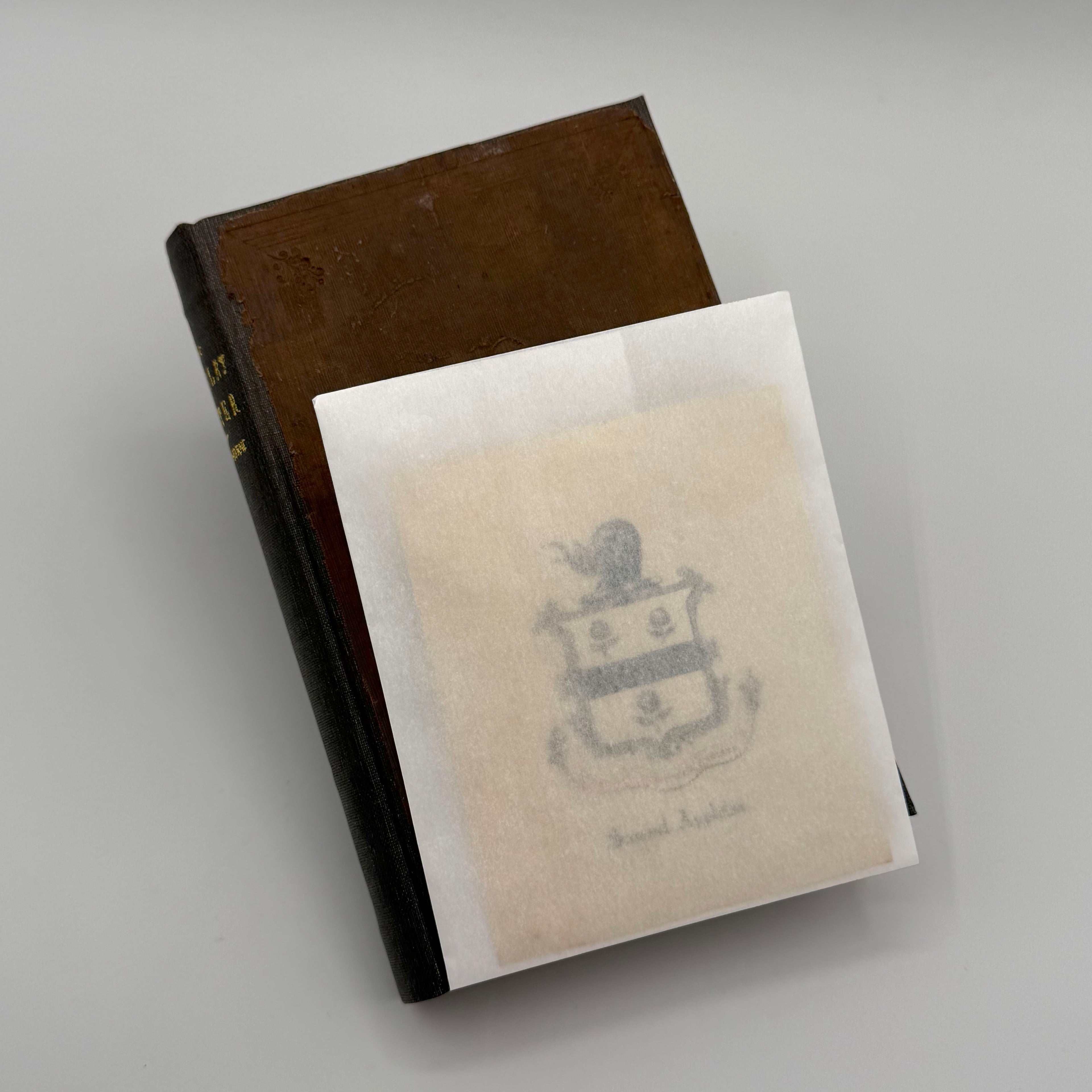 Brown book with a white paper cover featuring an emblem on a gray background