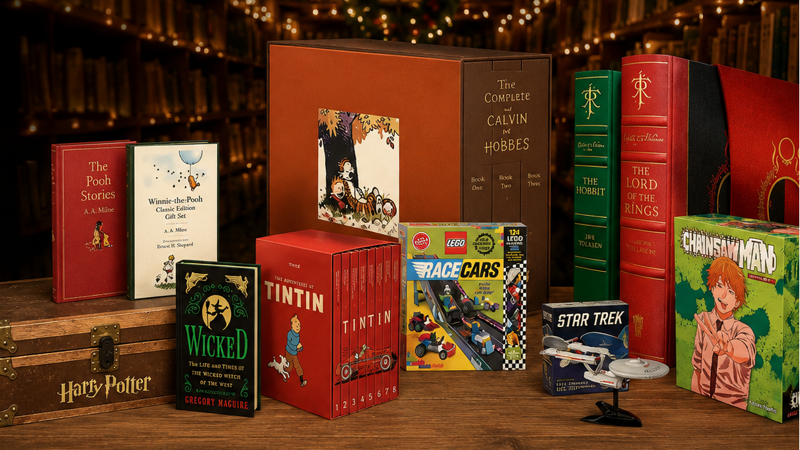 A curated collection of book boxes and boxed sets arranged on a wooden table in front of a dark library interior with string lights. Visible titles include Harry Potter, Wicked, The Tinted, The Complete Tin Tin, Star Trek, and The Chronicles of Narnia.