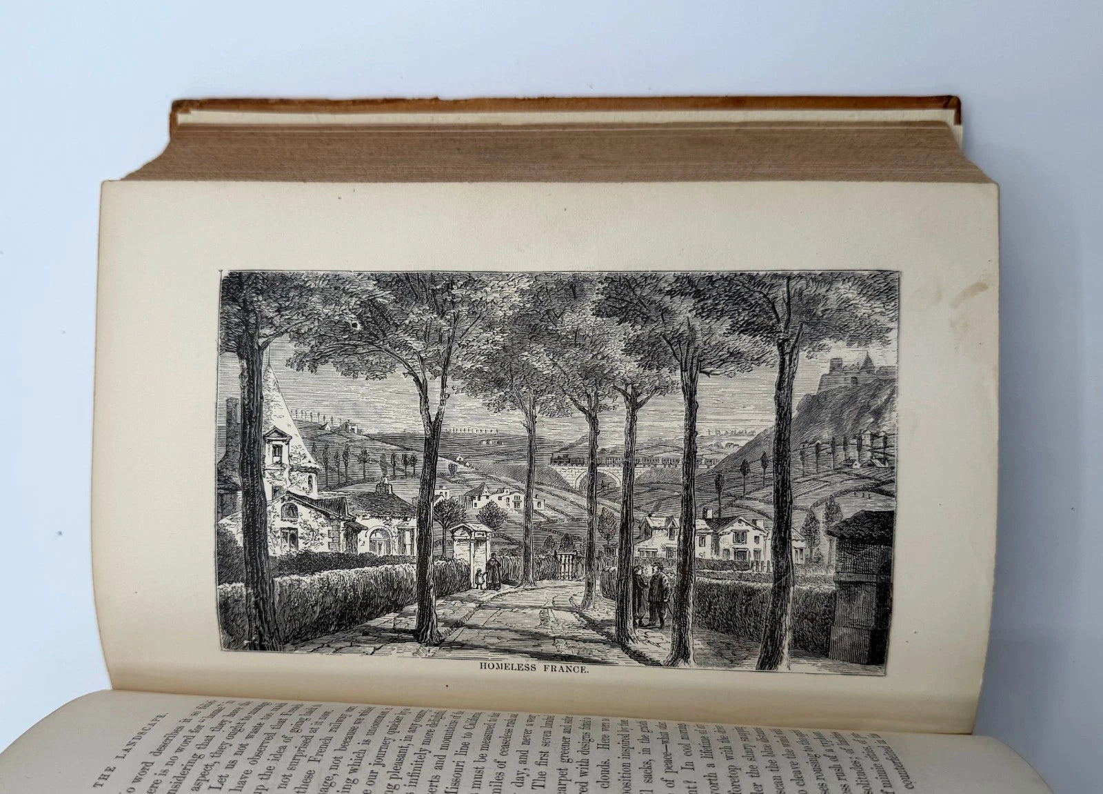 Open book with an engraved illustration of a village scene on a light blue background